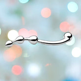 A gleaming metallic Njoy 'Fun Wand' Kegel Exerciser & P-Spot Stimulator, featuring a curved handle and a series of three spherical beads that gradually increase in size, culminating in a rounded tip, set against a blurred backdrop of vibrant lights.